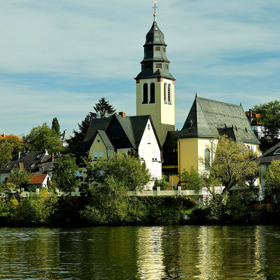 Bild vergr&ouml;&szlig;ern: Eine Kirche mit ihren Nebengebäuden, im Vordergrund ist ein Fluss zu sehen.